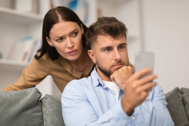 istock Jealous wife peeking over husband's shoulder as he texts indoors 1994912459
