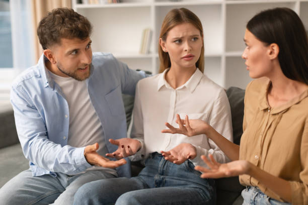 Three Angry Friends Having Quarrel Sitting On Sofa At Home