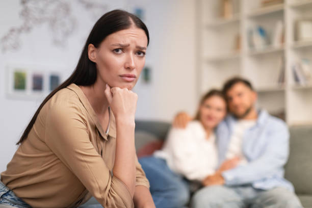 couple embraces while unhappy young lady looking at camera indoor Millennial couple embraces on couch while unhappy young lady looking at camera, suffering from loneliness and jealousy, complexity of friendship relationships between lonely and married friends jealous ex girlfriend stock pictures, royalty-free photos & images
