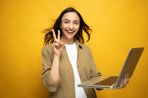 Portrait of young woman using laptop isolated yellow background