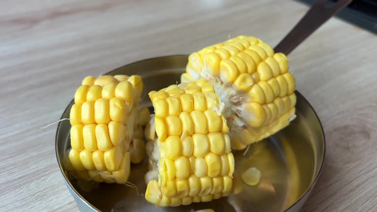 Sweet Yellow Corn Fresh Boiled and Hot on a Plate on Lunch Table in Kitchen Putting steamed corn cobs on a plate piece of sweet corn and seeds closeup