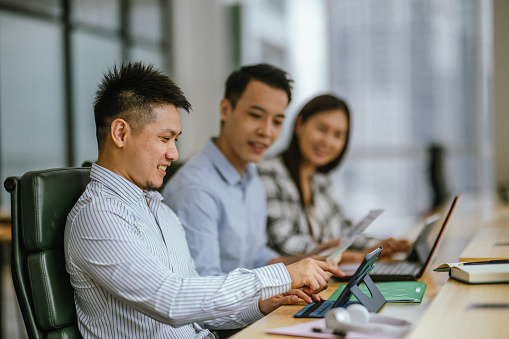 An Asian Male Business Leader and His Advisory Team Engaged in Discussion in a Modern Office Setting