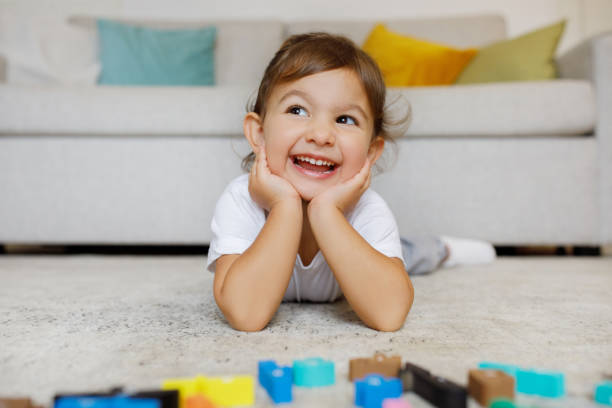 Dreamy Cute Toddler Girl Lying On Floor In Living Room Interior Dreamy Cute Toddler Girl Lying On Floor In Living Room Interior, Adorable Preschooler Female Child Resting Head On Hands And Looking Away, Relaxing At Home After Playing With Development Toys sorter machine stock pictures, royalty-free photos & images