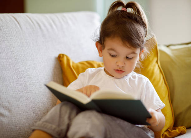 istock Small child relaxing on couch with book, experiencing the joy of reading 1994947691