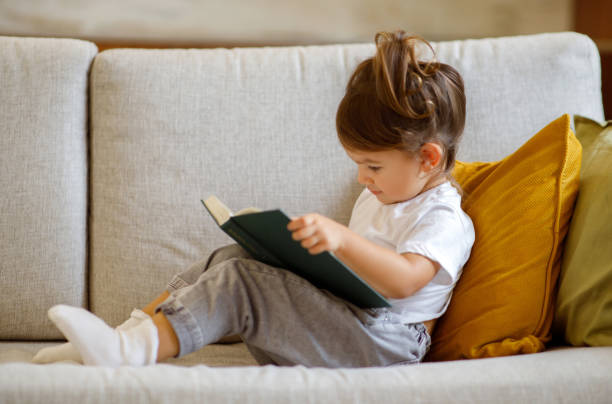 istock Cute Little Girl Relaxing On Couch With Interesting Book 1994947739