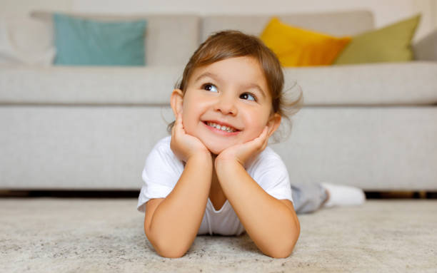 Cheerful cute little girl daydreaming on the floor at home stock photo