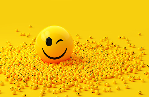 Yellow spheres textured with happy face emoji surrounded by other happy face emojis on yellow background. Horizontal composition.