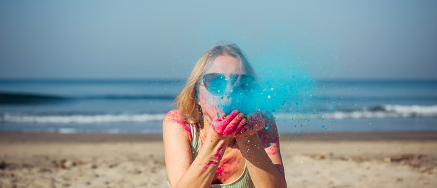 A beautiful girl on the seashore in a multicolored Holi powder smiles and waves her hands at the Holi Festival. Tourist trips to India for the Happy Holi Festival.