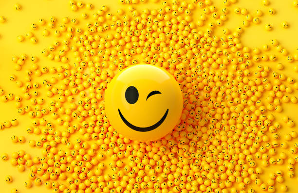 Yellow spheres textured with happy face emoji surrounded by other happy face emojis on yellow background. Horizontal composition.