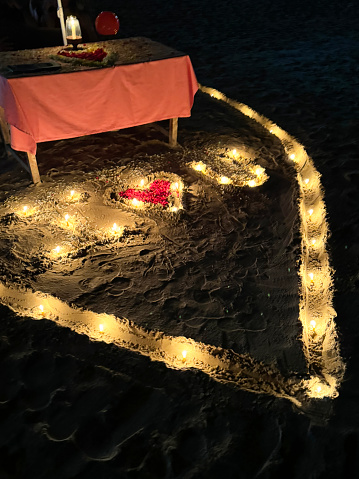 Stock photo showing beachfront restaurant illuminated at night by tea light candles in heart-shaped hole made by digging shape in the sand of beach.