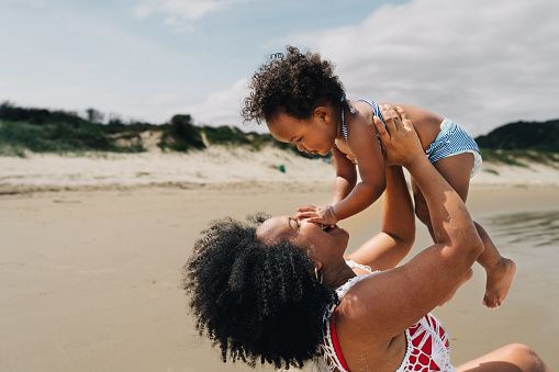 Loving mom playing with her baby girl on a beach in summer