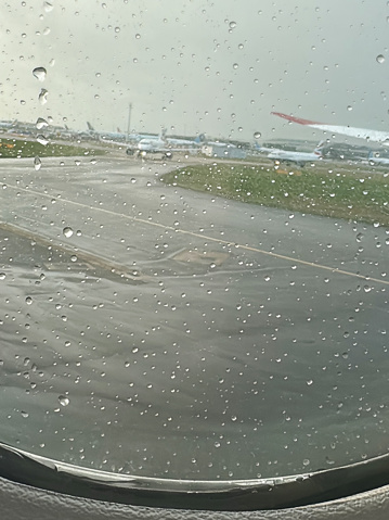 Stock photo showing grounded planes pictured on aeroplane apron tarmac viewed through the cabin window, covered in rain drops, of recently landed airplane.