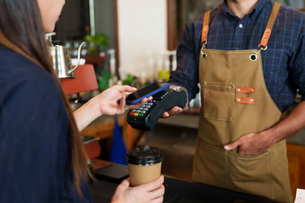 istock Male cafe employees various nationalities holding credit card acceptor QR code smiled. brunette female customer holding mobile phone scan payments holding disposable paper coffee cup small business. 1995023391