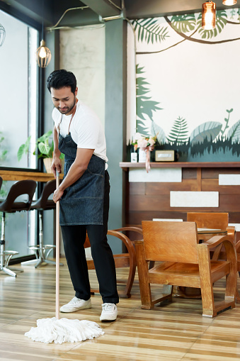 Handsome Spanish coffee shop worker mopping coffee shop floor after closing small business Family restaurants and to prepare to accommodate customers who come to use the service the next day.