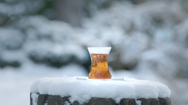 Pouring black tea in cups at winter snowy day outdoors. Filling Turkish tea in cup from teapot. Snow is falling. Cups of hot drink