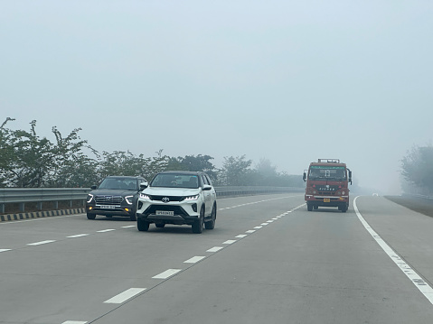 Delhi, India - January 3, 2024: Stock photo showing view from car rear windscreen of traffic; lorry, cars and taxis seen travelling in a polluted foggy tailback on a multilane highway.