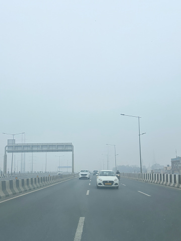 Delhi, India - January 16, 2024: Stock photo showing view from car rear windscreen of traffic; motorcycles, cars and taxis seen travelling in a polluted foggy tailback on a multilane highway.