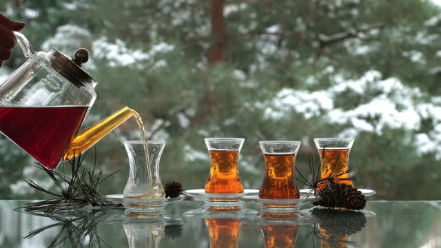 Pouring black tea in cups at winter snowy day outdoors. Filling Turkish tea in cup from teapot. Snow is falling. Cups of hot drink
