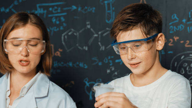 istock Caucasian boy mixing chemical liquid while teacher giving advice. Erudition. 1995050886