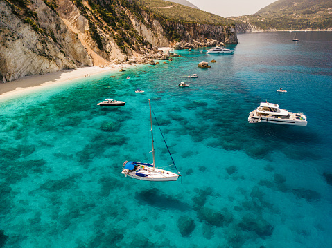 A beautiful bay with sailboats and catamaran on island of Ithaca, Greece. There are sailboats, one catamaran and one yacht anchored in the bay. The sea is crystal clear, blue and turquoise.