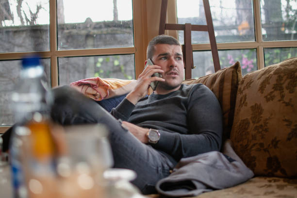 istock a young man is sitting on a sofa by the window and talking on a mobile phone 1995060479