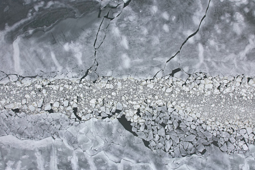 Frozen sea ice cracked by a boat from above