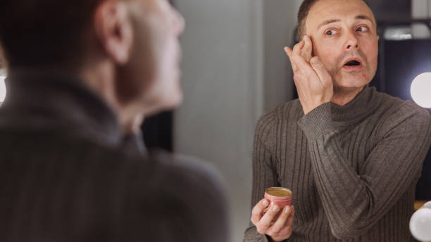 istock Metrosexual Caucasian man applying an face cream while observing himself in the mirror 1995077528
