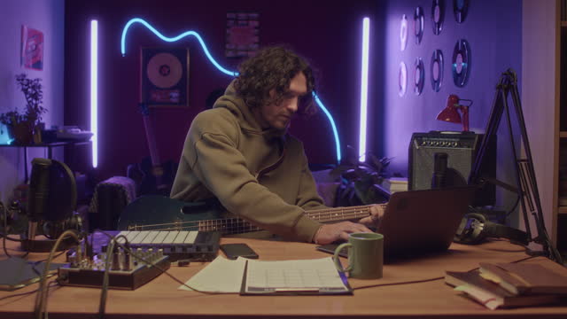 Man Tuning Guitar Using Laptop at Home Recording Studio at Night