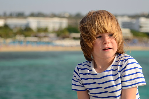 A cute boy enjoys the sea, in the background there is the coast and beaches, the beautiful color of the sea. Family trip. Vacation with children. Tourists on the island