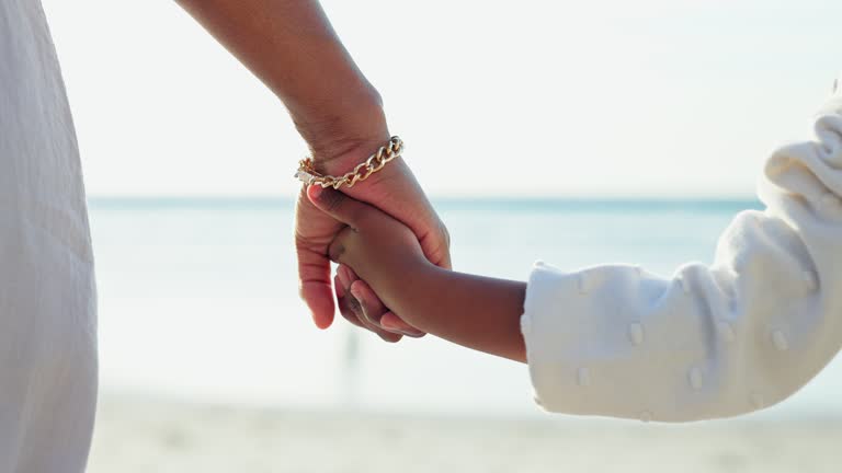 Mother, child and holding hands in closeup at beach for bond, trust or care on vacation, travel or trip. Woman, kid and together for safety, security or support on adventure to ocean, coast or sea