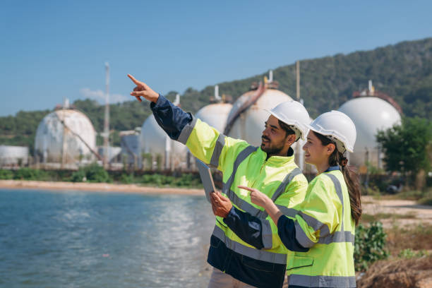 istock Engineer using a tablet and gesturing towards an industrial facility under a clear blue sky. 1995115159