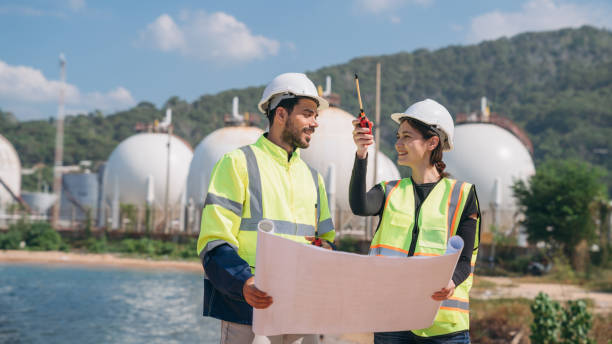 istock Two engineers in safety gear with blueprints discussing work in front of industrial storage tanks on a clear day. 1995115782