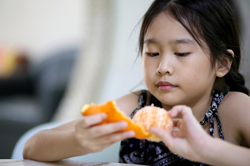 Portrait of young Asian girl peeling tangerine fruit at home