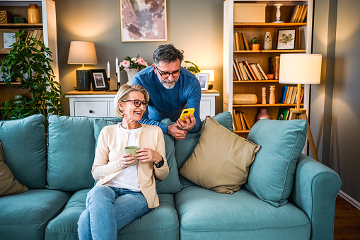 Cheerful mature couple looking at mobile phone at home