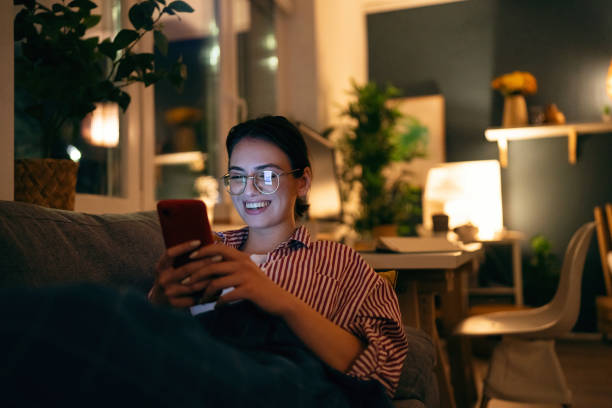 istock Young smiling woman using her phone during the relaxing evening at home 1995158416