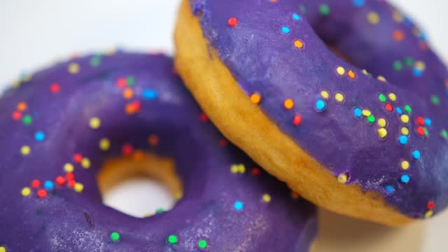 Two lilac blueberry donuts with multi-colored confectionery sprinkles
