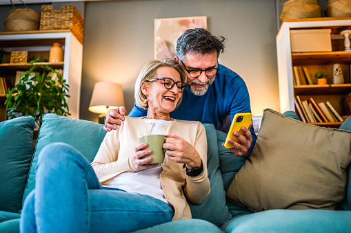 Cheerful mature couple looking at mobile phone at home