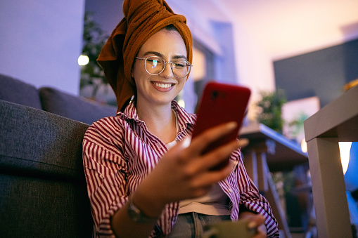 Young smiling woman using her phone during the relaxing evening at home.