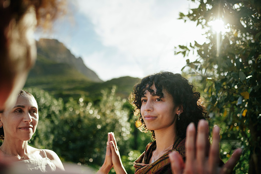 Young woman and a group of other women standing with her hands together during an outdoor exercise at a wellness retreat in summer