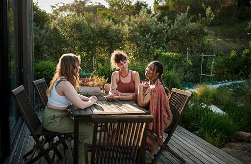Group of diverse women supporting each other while talking together around a patio table outside during a summer wellness retreat