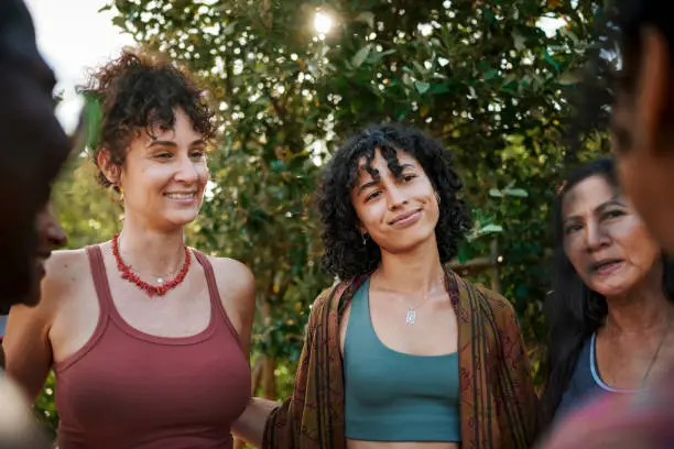 Diverse group of smiling women standing arm in arm together in a circle outside during a session at a wellness retreat in summer