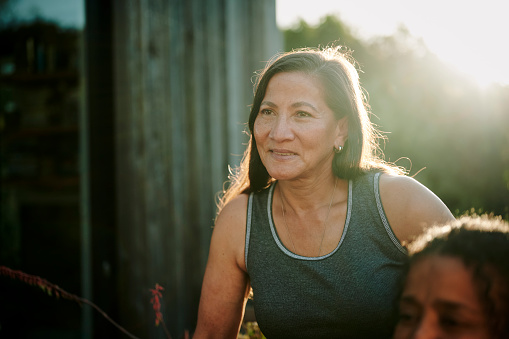 Mature woman smiling while sitting outside with a diverse group of other women during a wellness retreat in summer