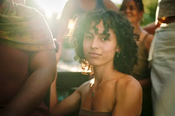 Portrait of a young woman sitting outdoors with a diverse group of other women during a wellness retreat in summer