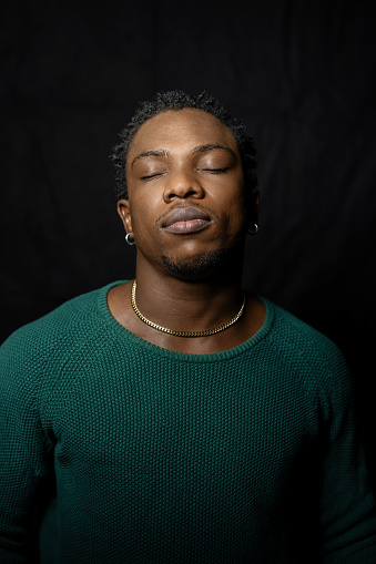 African man with closed eyes against black background. Young African male model thinking with his eyes closed in studio.