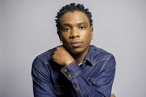 Portrait of thoughtful young african man looking at camera. African male in denim shirt staring at camera against gray background.