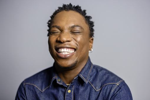 Close-up of cheerful african man against grey background. African male in blue denim shirt smiling in studio.