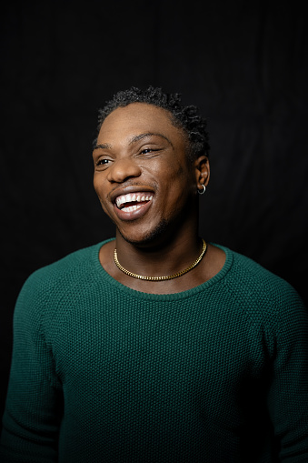Portrait of laughing young man on black background. Smiling young male looking away.