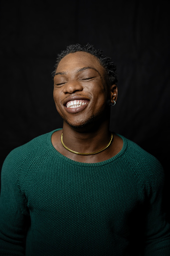 Portrait of african young man smiling with eyes closed. Smiling young male on black background.