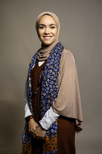 Portrait of cheerful young Islamic woman smiling on brown background. Muslim female wearing hijab smiling at camera in studio.