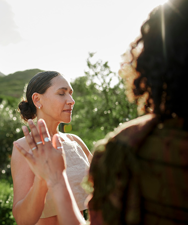 Mature woman standing with her eyes closed and hands together with a group of women during an exercise at a wellness retreat in summer